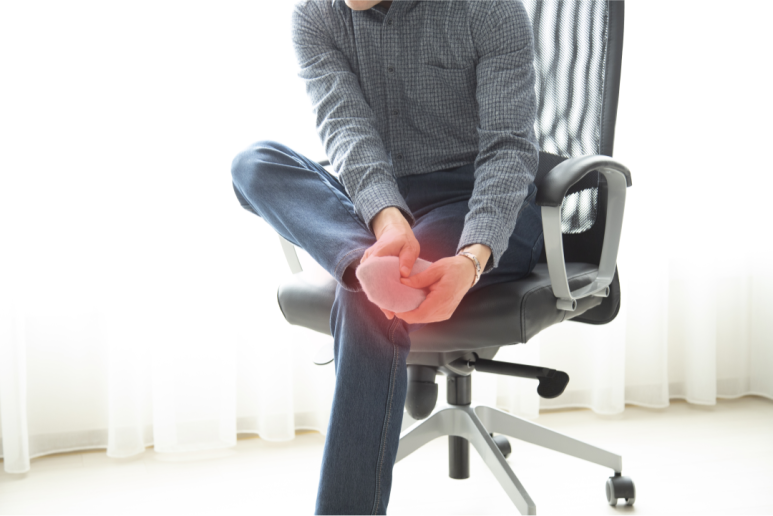 족저근막염으로 아픈 남자가 의자에 앉아 한쪽 다리를 다른 다리 위에 올린 사람이 발목 부위를 두 손으로 잡고 있다. 발목 부분이 붉게 강조되어 통증이나 염증이 있음을 나타낸다. 밝은 실내에서 촬영된 장면이다. 분당 정자역 라룬리픽스
