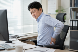 40대 직장인이 사무실에서 의자에 앉아 허리를 잡으며 뻐근함을 느끼는 장면 라룬리픽스